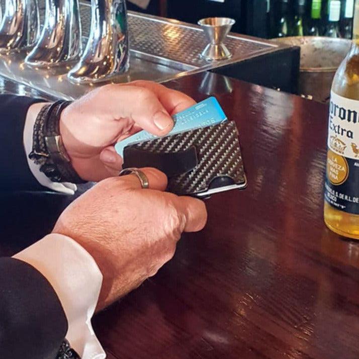 Man holding carbon fibre RFID wallet while paying for a beer